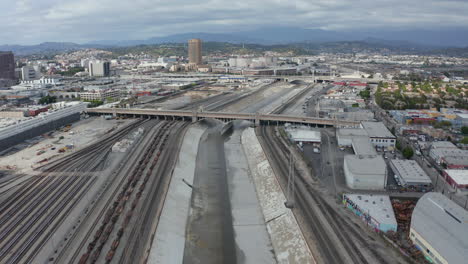 AERIAL:-Los-Angeles-River-with-Water-on-Cloudy-Overcast-Sky-next-to-Train-Tracks